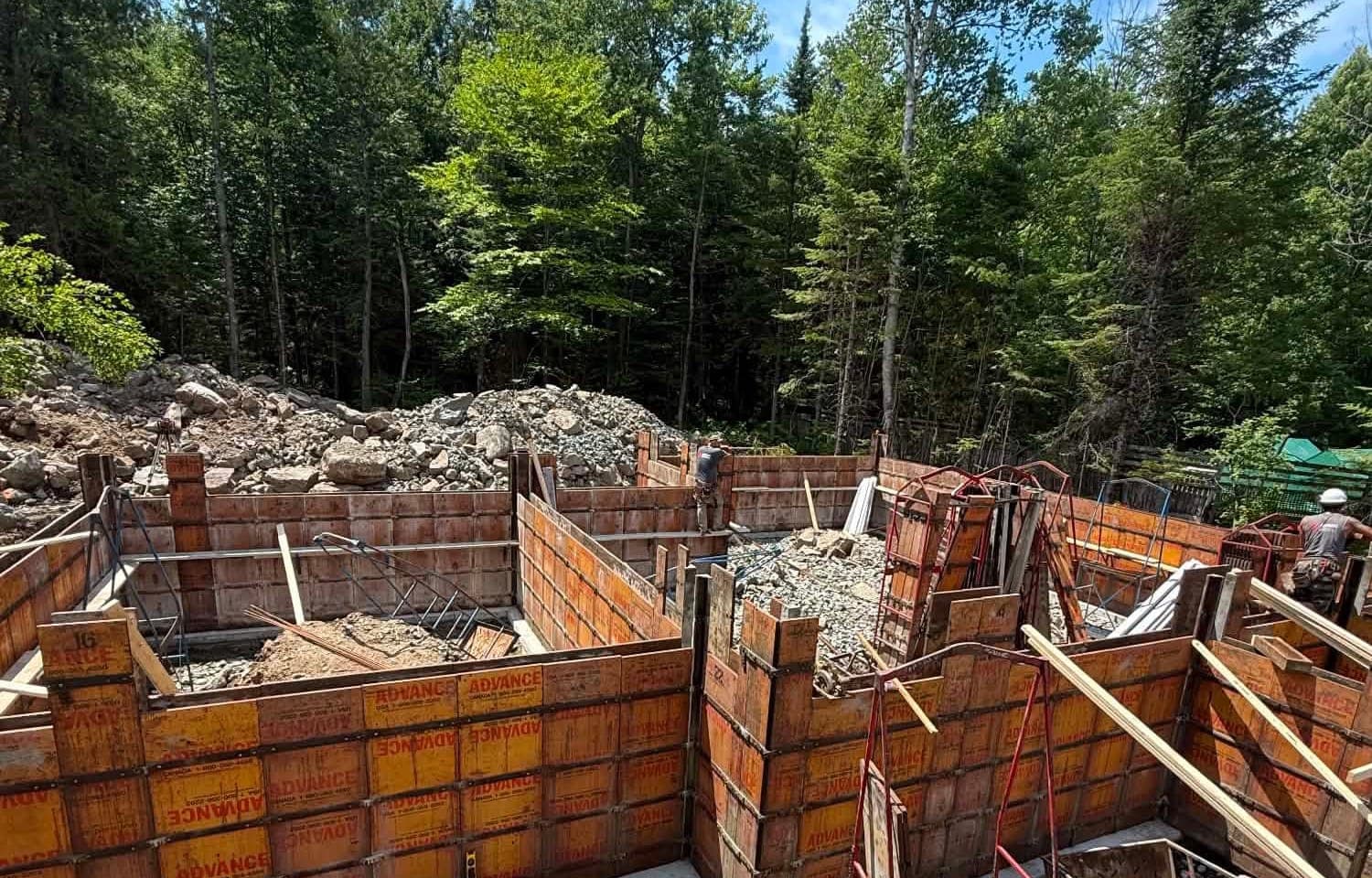 Les coffrages orange d’une fondation de maison en construction, au milieu d’un terrain boisé