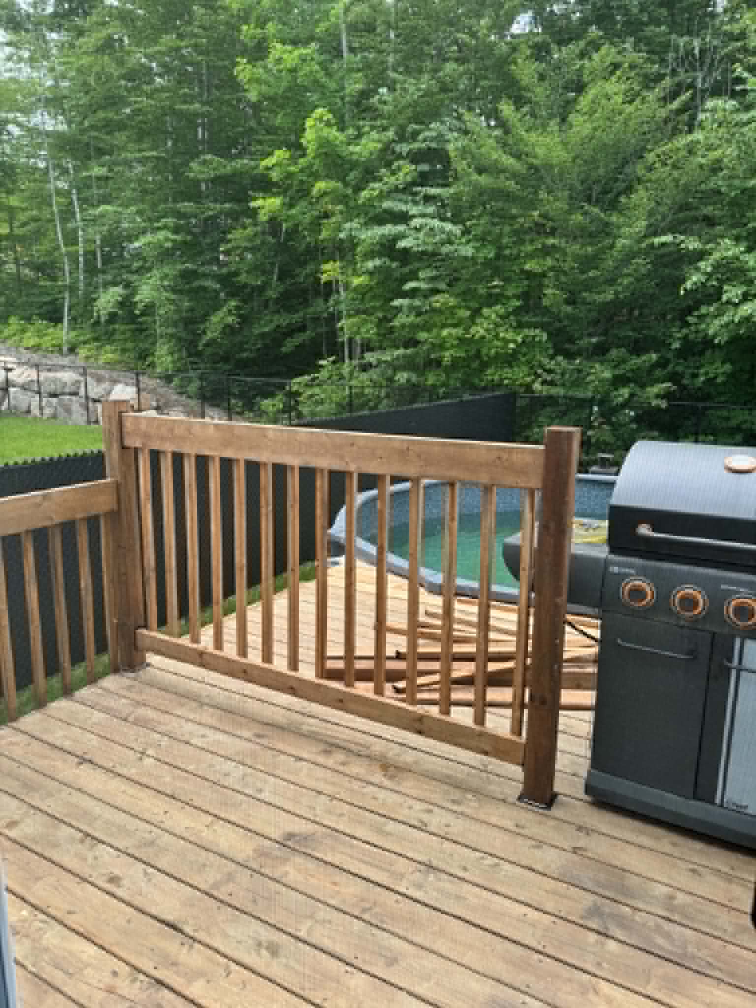 Le patio fini avec son garde-corps et sa barrière en bois traité, à côté de la piscine hors terre.