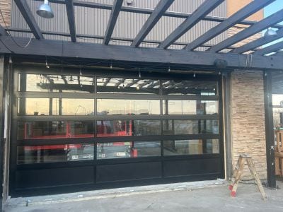 Grande porte de garage pleine vue en aluminium et verre installée sur un local commercial avec pergola
