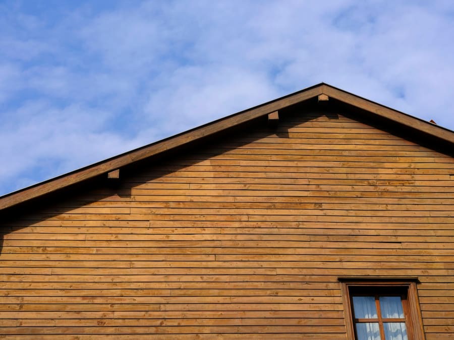 Pignon d’une maison recouvert de planches de cèdre naturel posées à l’horizontale, sous un ciel bleu