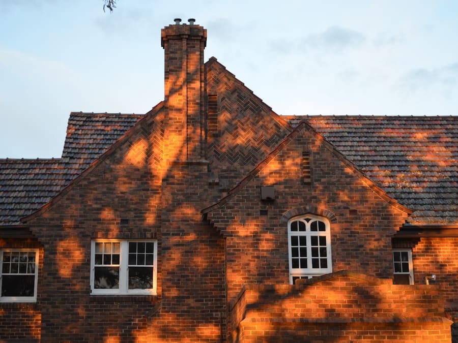Façade de maison en brique rouge avec un pignon et une cheminée, éclairée par le soleil de fin de journée